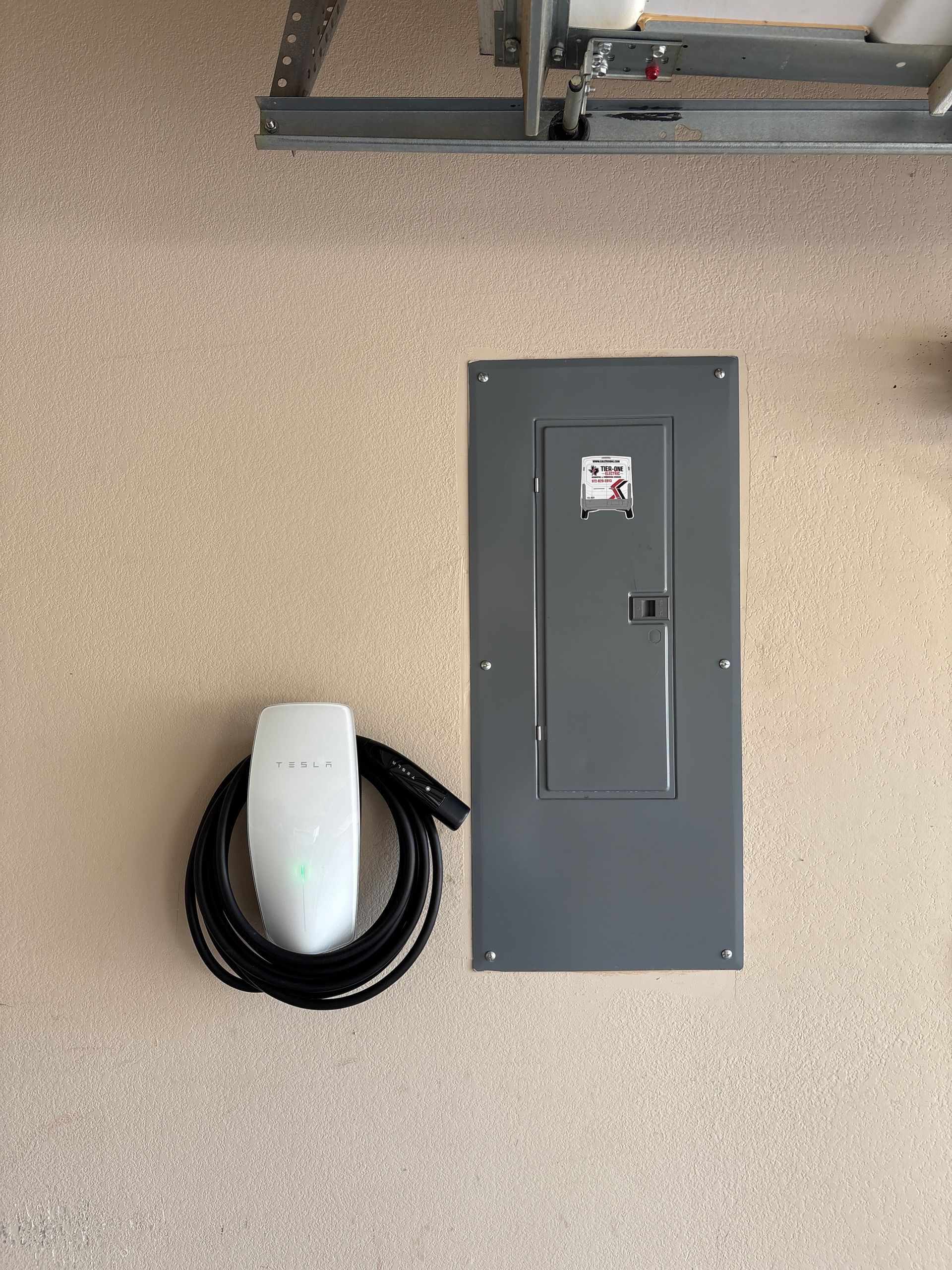 Wall-mounted electrical panel on a beige wall with a coiled black cable and white protective cover beside it.