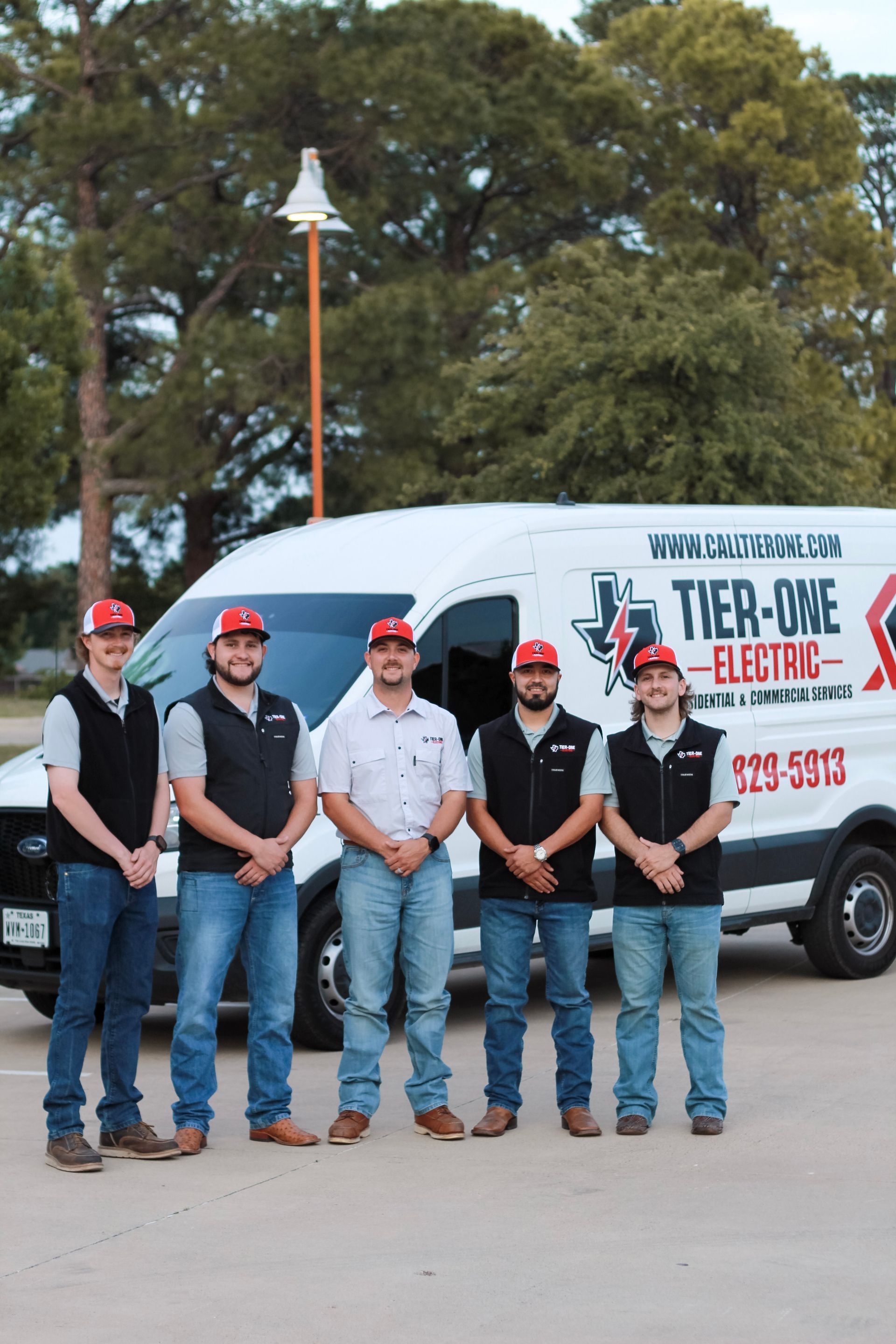 Five workers in hard hats stand in front of a white service van outdoors.
