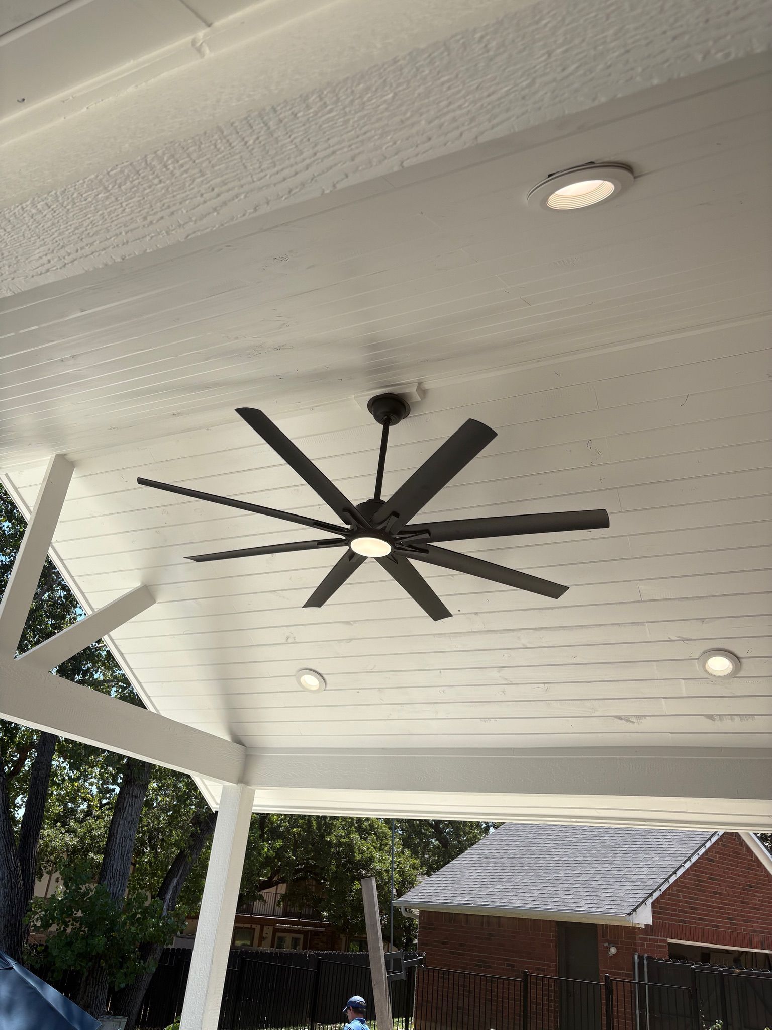 Covered patio ceiling with a large black ceiling fan and recessed lights