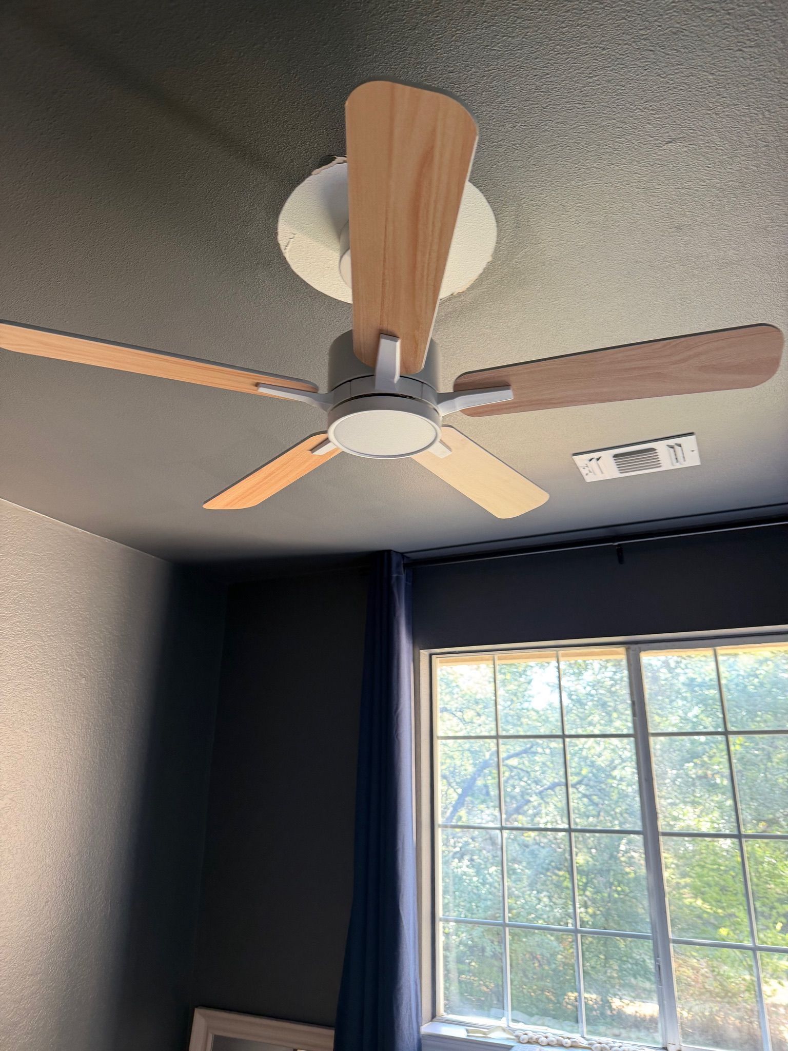 Ceiling fan with wood blades above a window with dark curtains in a room