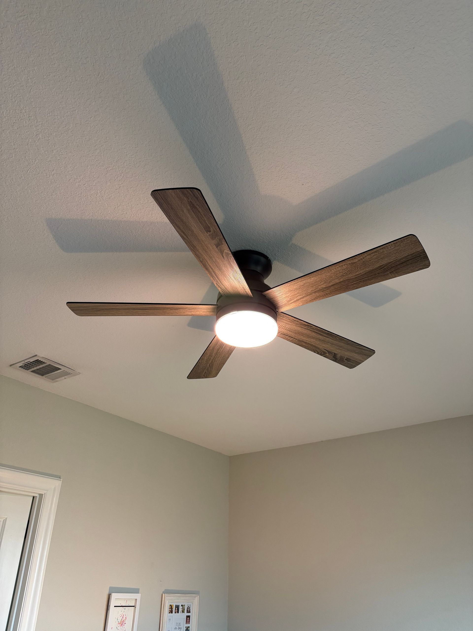 Ceiling fan with wooden blades and a lit light fixture in a room corner.