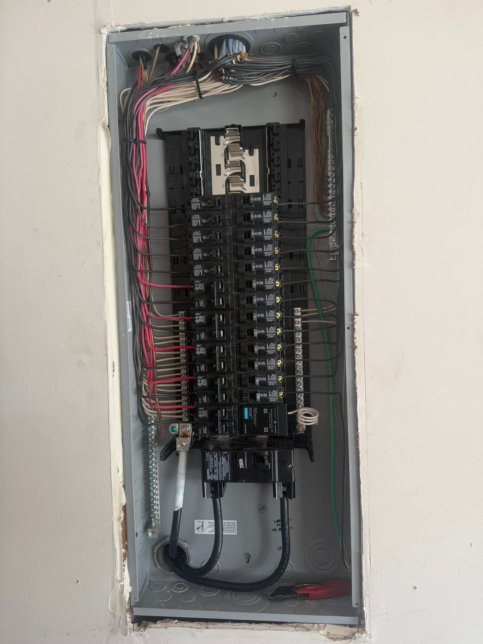 Open electrical breaker panel with exposed wiring in a wall recess