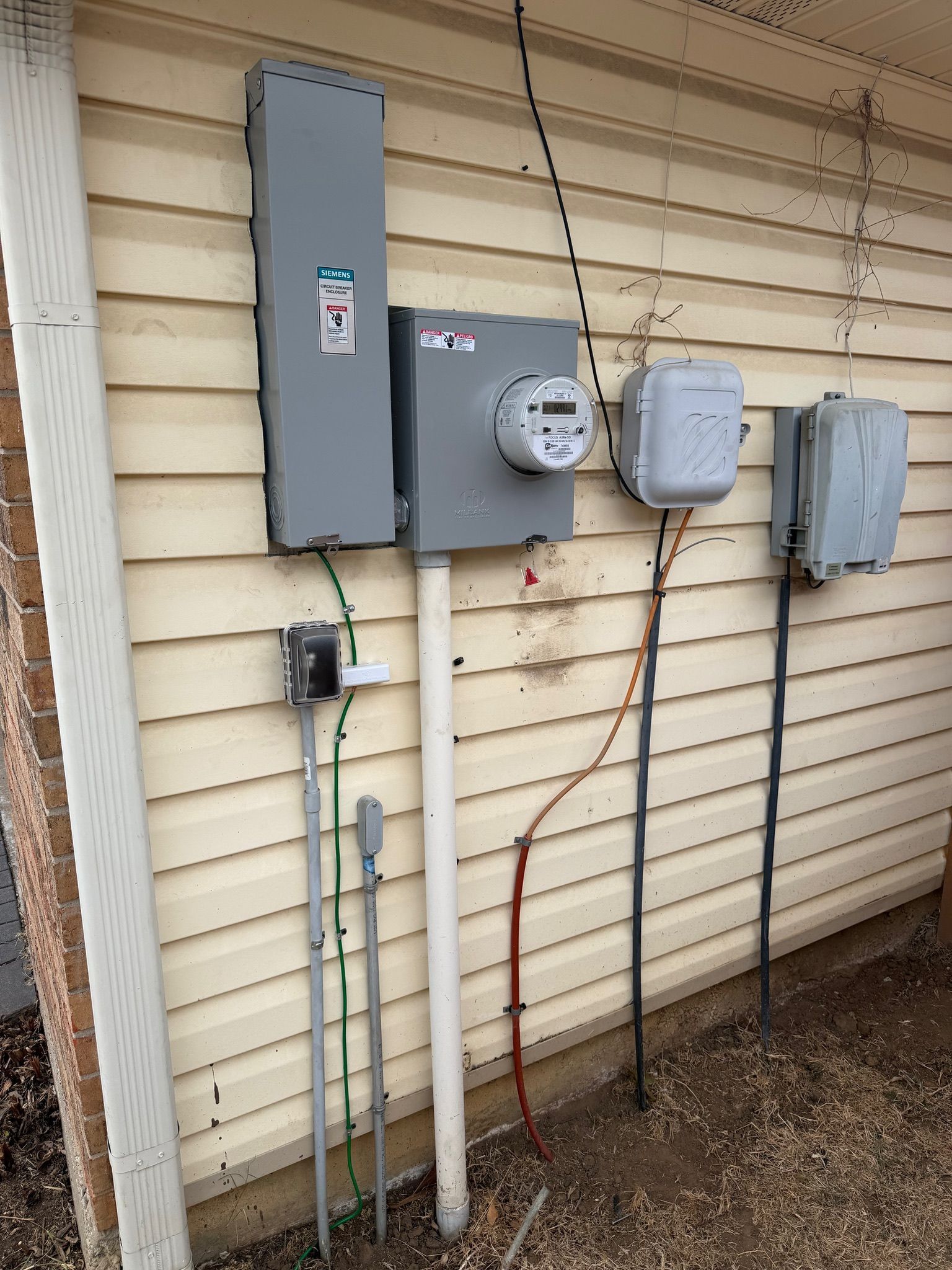 Electric meters and utility boxes mounted on a beige house exterior wall.