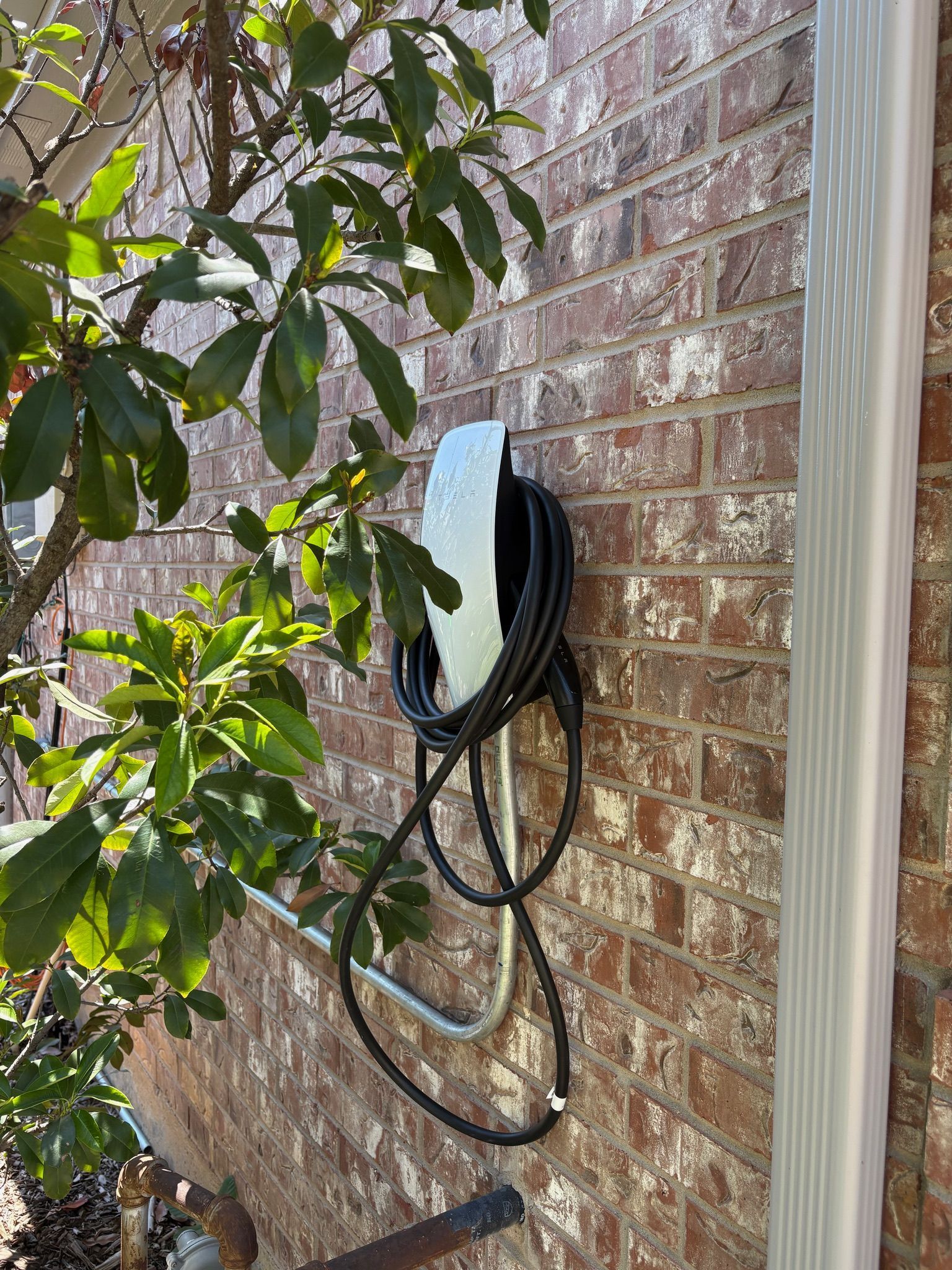 Black wall-mounted cable box on a brick house exterior, with coiled black cords nearby.