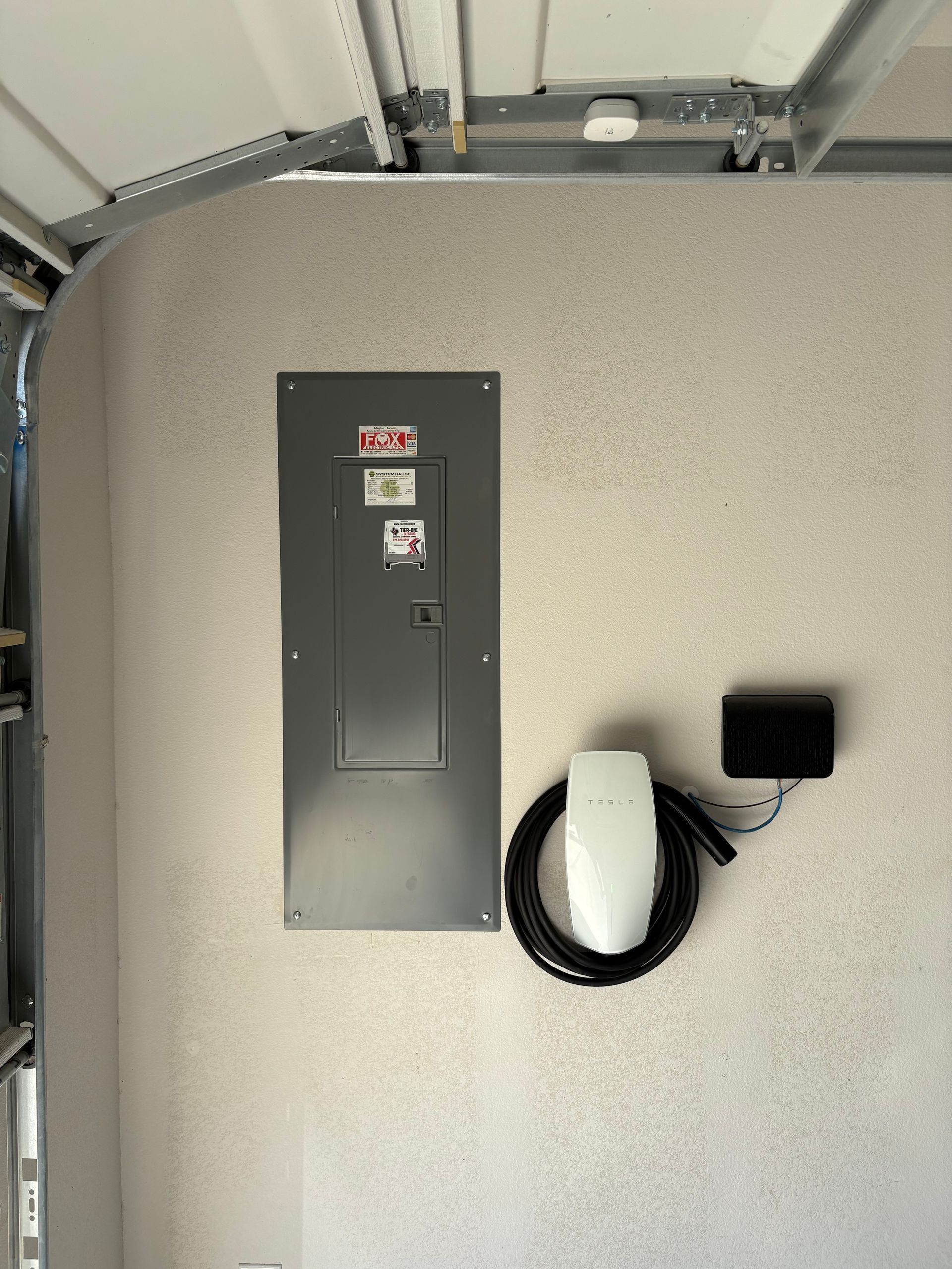 Gray utility panel on a speckled wall with coiled black cable and small black device beside it