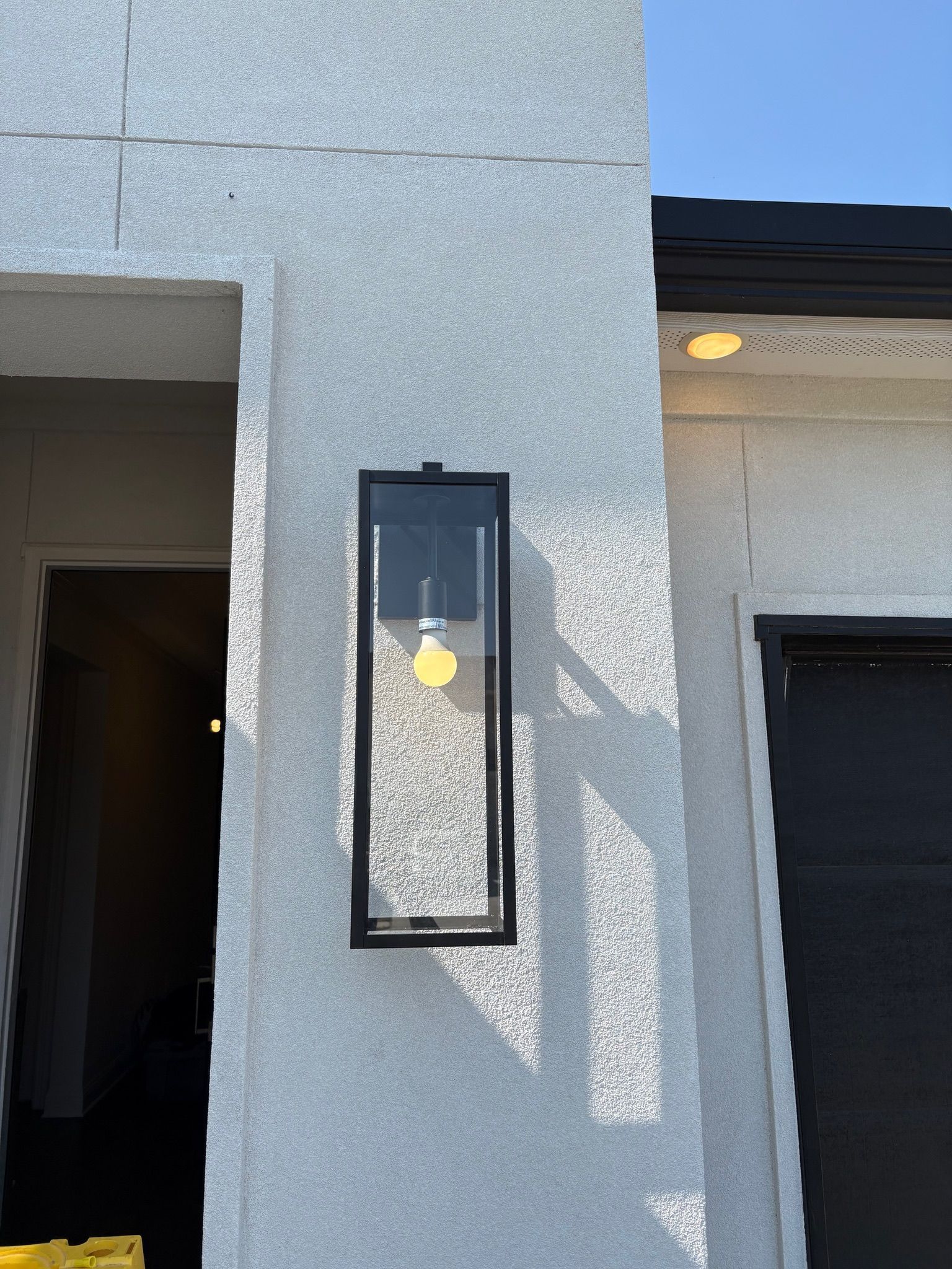 Exterior wall with a black lantern-style light fixture and a shadow cast on white stucco.