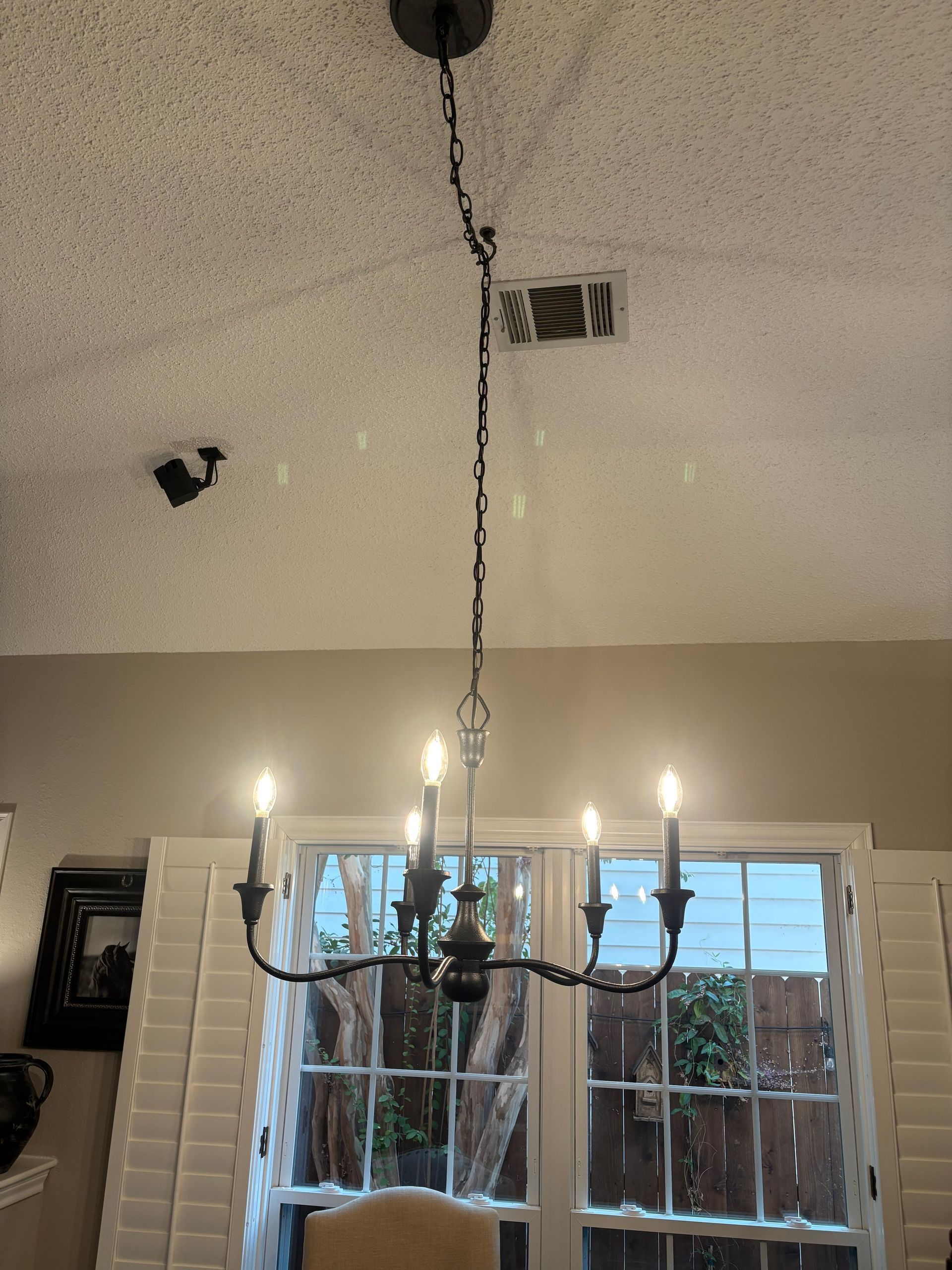 Black chandelier hanging from a textured ceiling above a window with white shutters