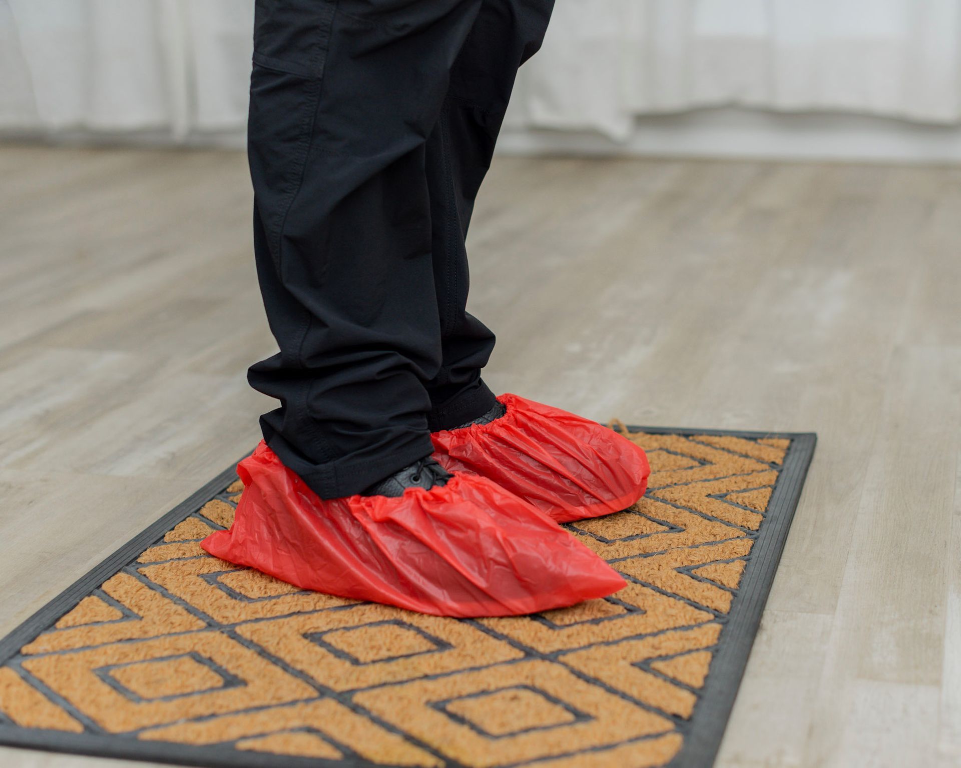 Person wearing red shoe covers stands on a patterned doormat indoors.