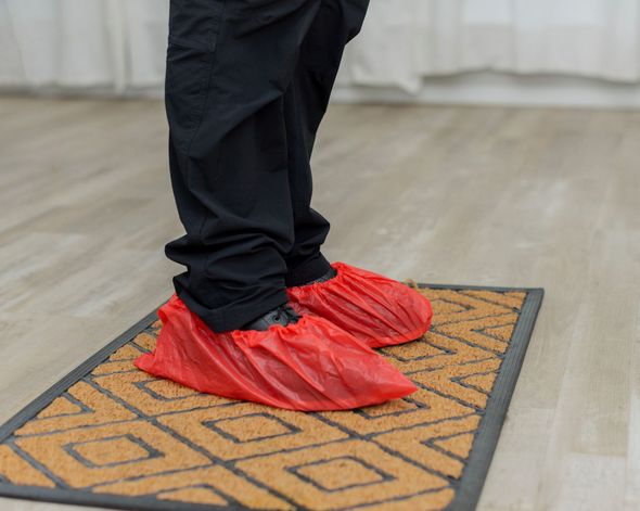 Person wearing red shoe covers stands on a patterned doormat indoors.