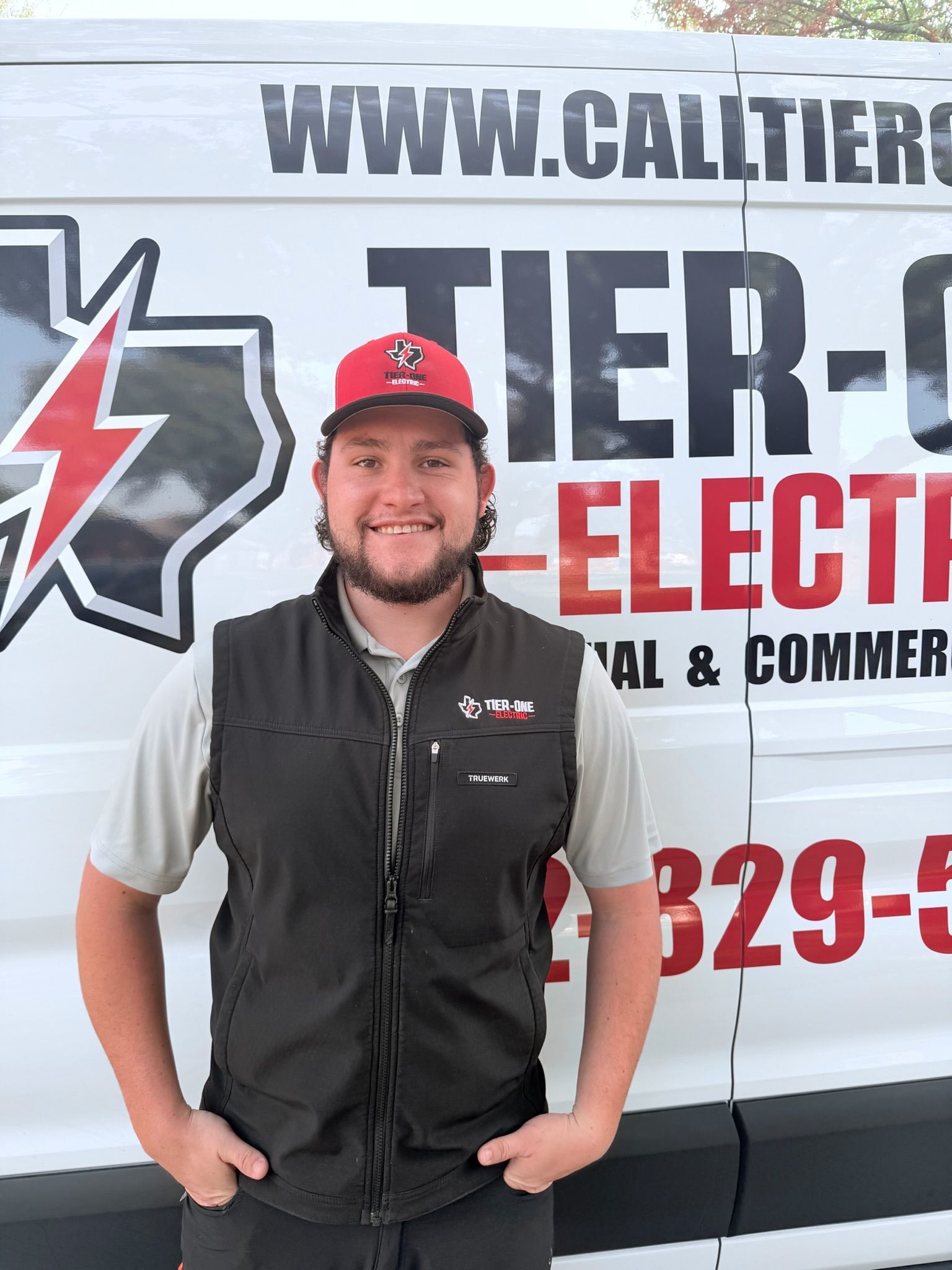 Man in vest and cap, smiling in front of a van with 