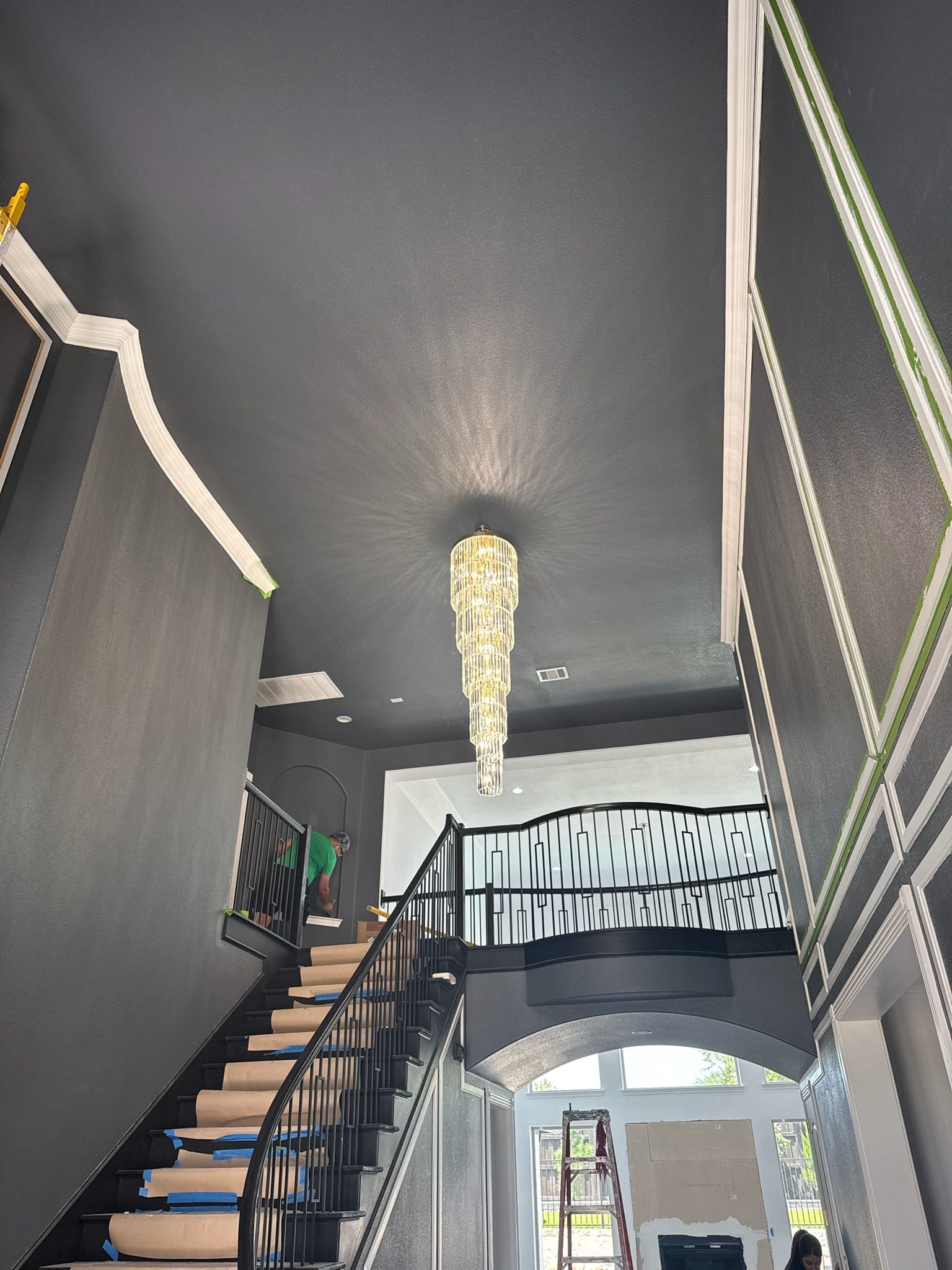 A staircase leads up to a hallway with a chandelier. Dark gray walls and ceiling, white trim.