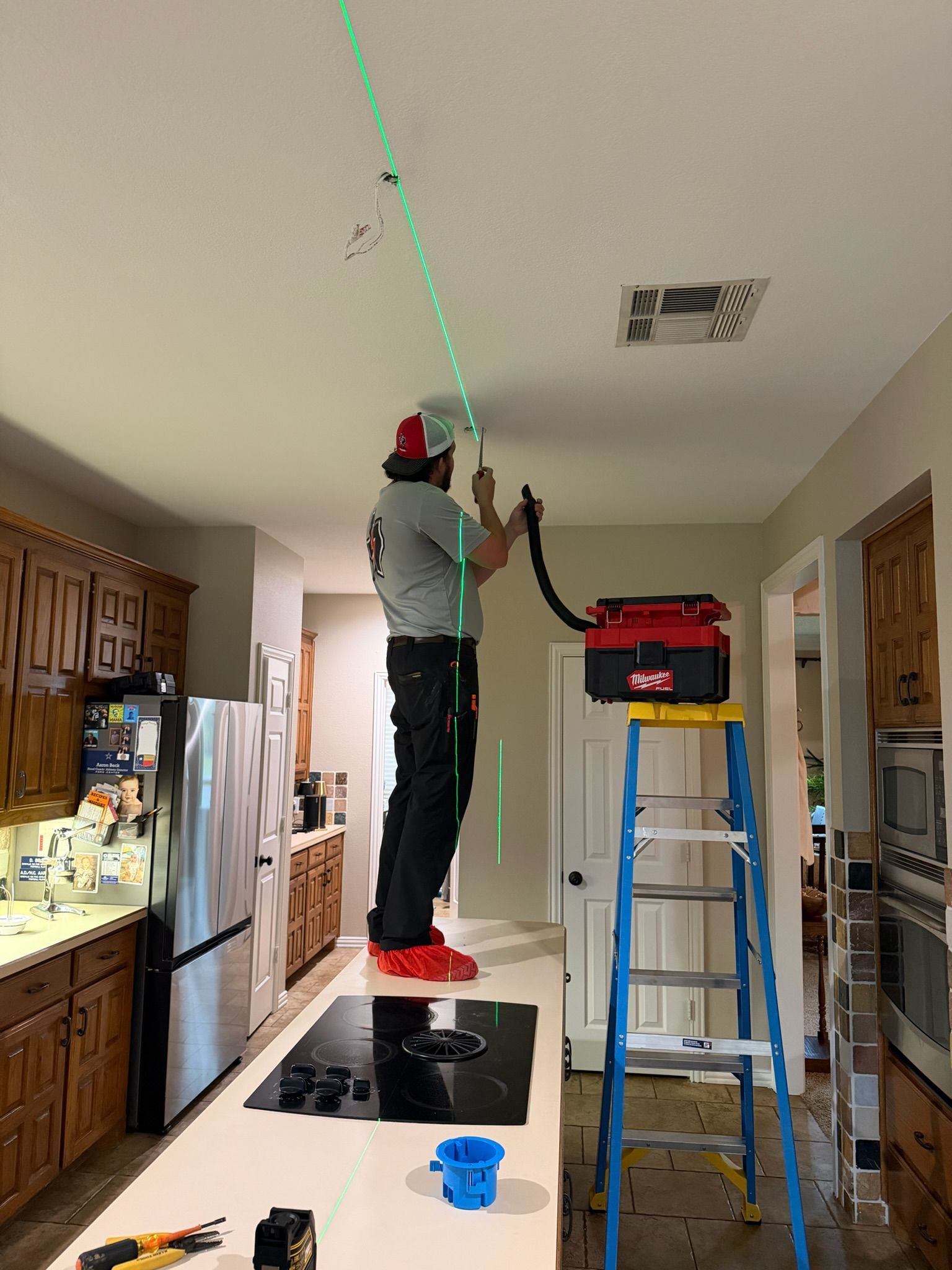 Tier-One Electric technician using laser alignment while installing a kitchen ceiling light fixture.