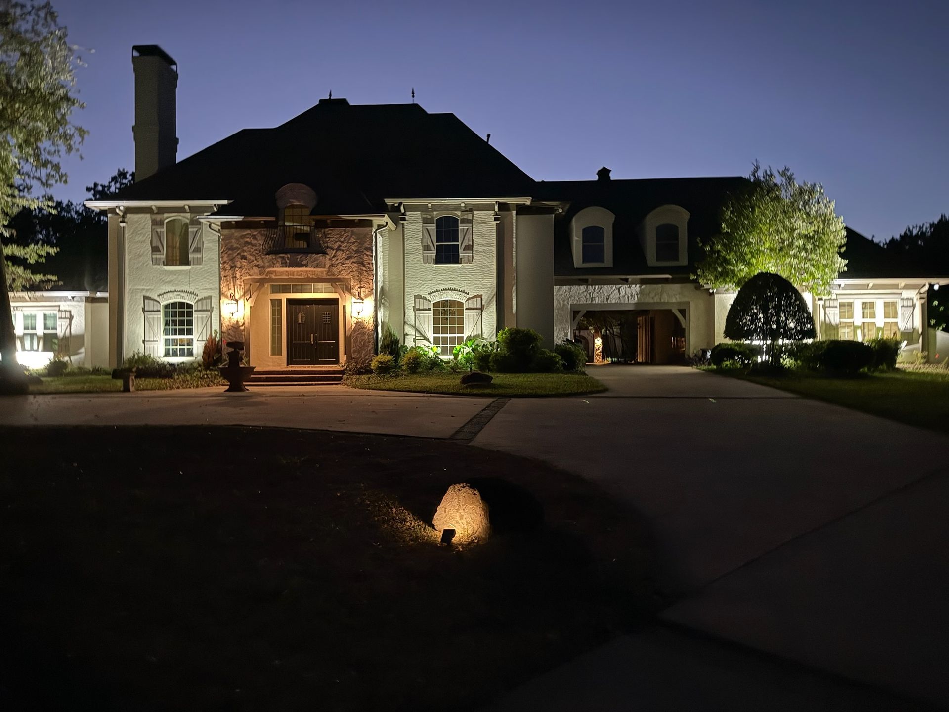 Residential landscape uplighting illuminating the exterior of a large home at night by Tier-One Electric.