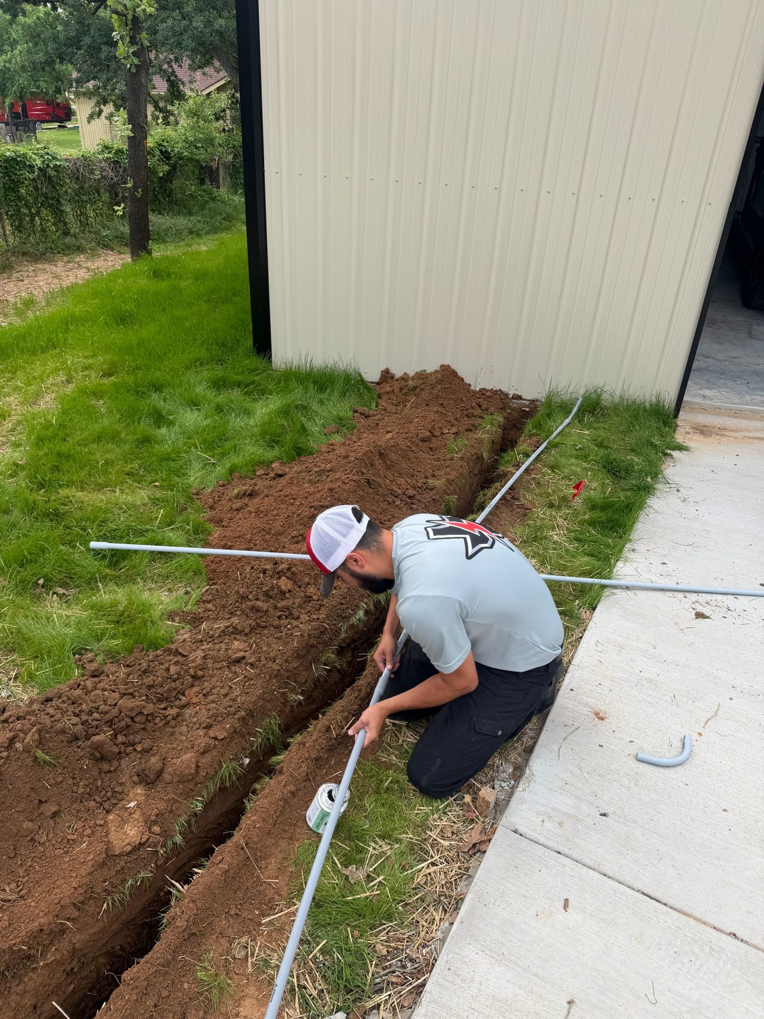Tier-One Electric technician installing underground electrical conduit in a residential trench.