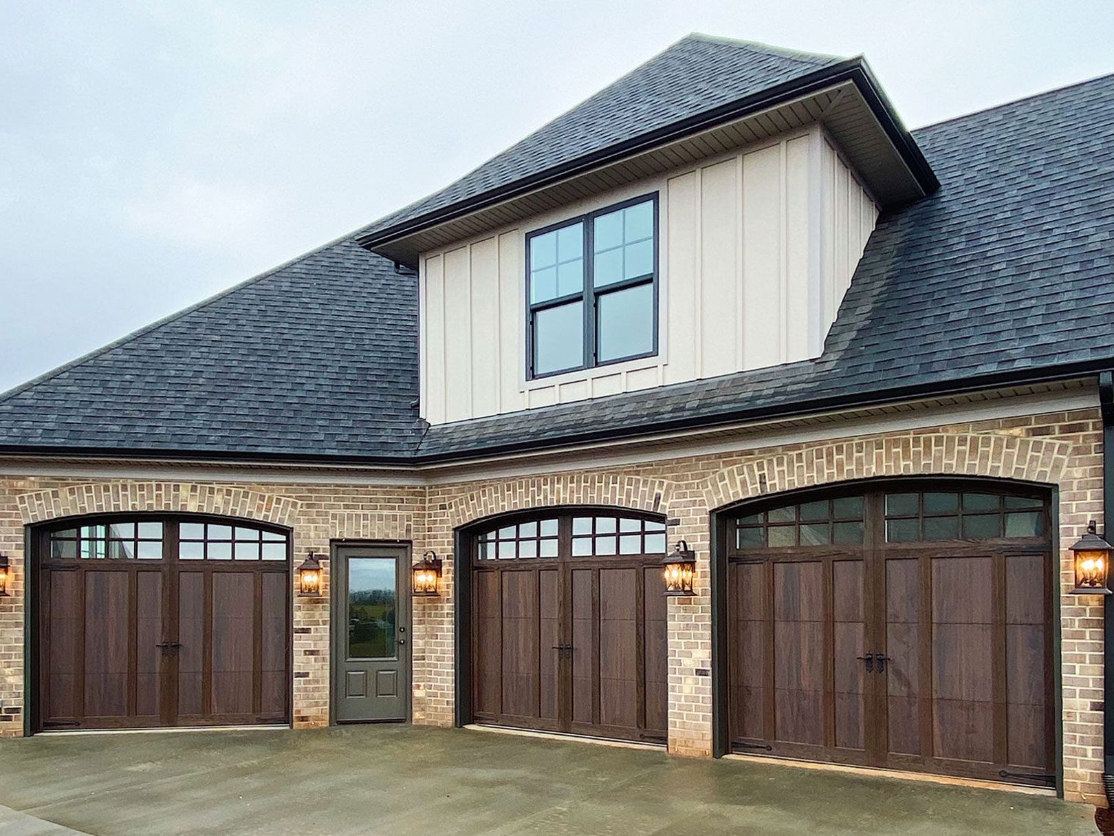 A large house with three garage doors and a window on the top of it.