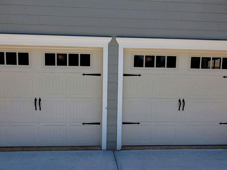 Two white garage doors with black handles on a house