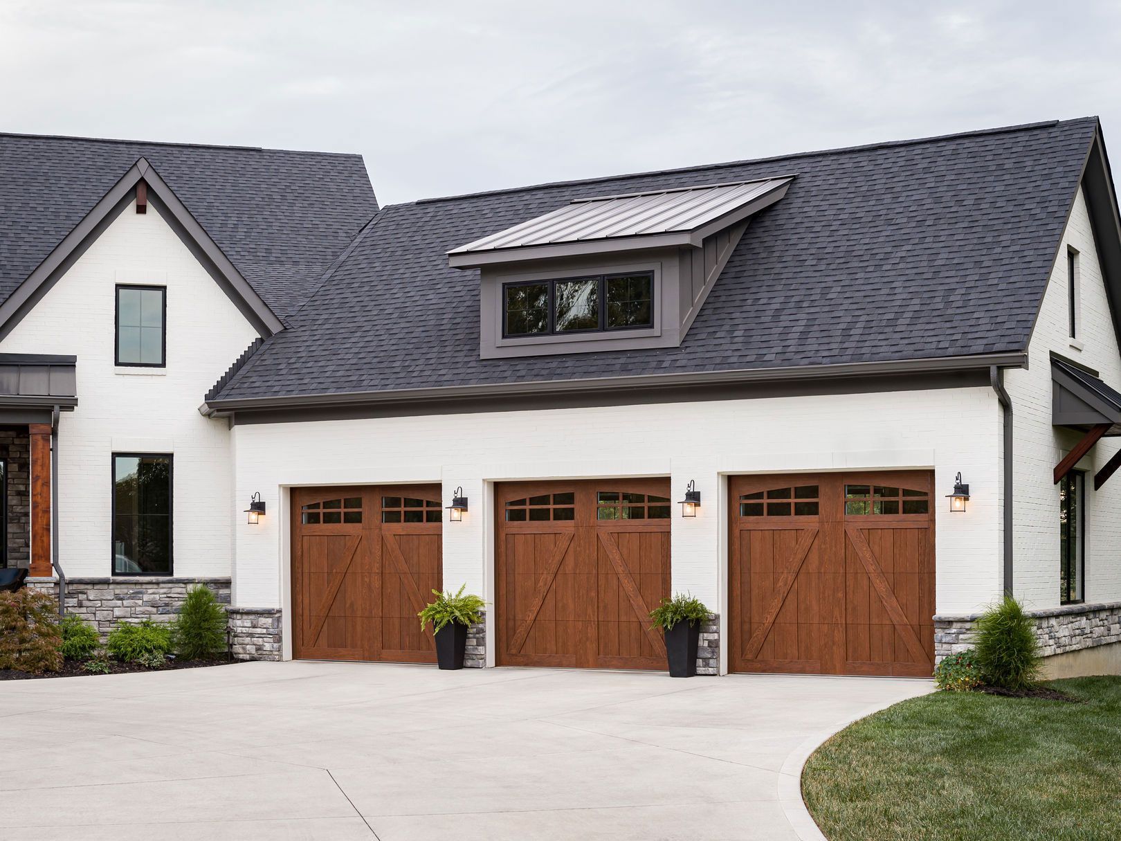 A white house with three wooden garage doors and a black roof.