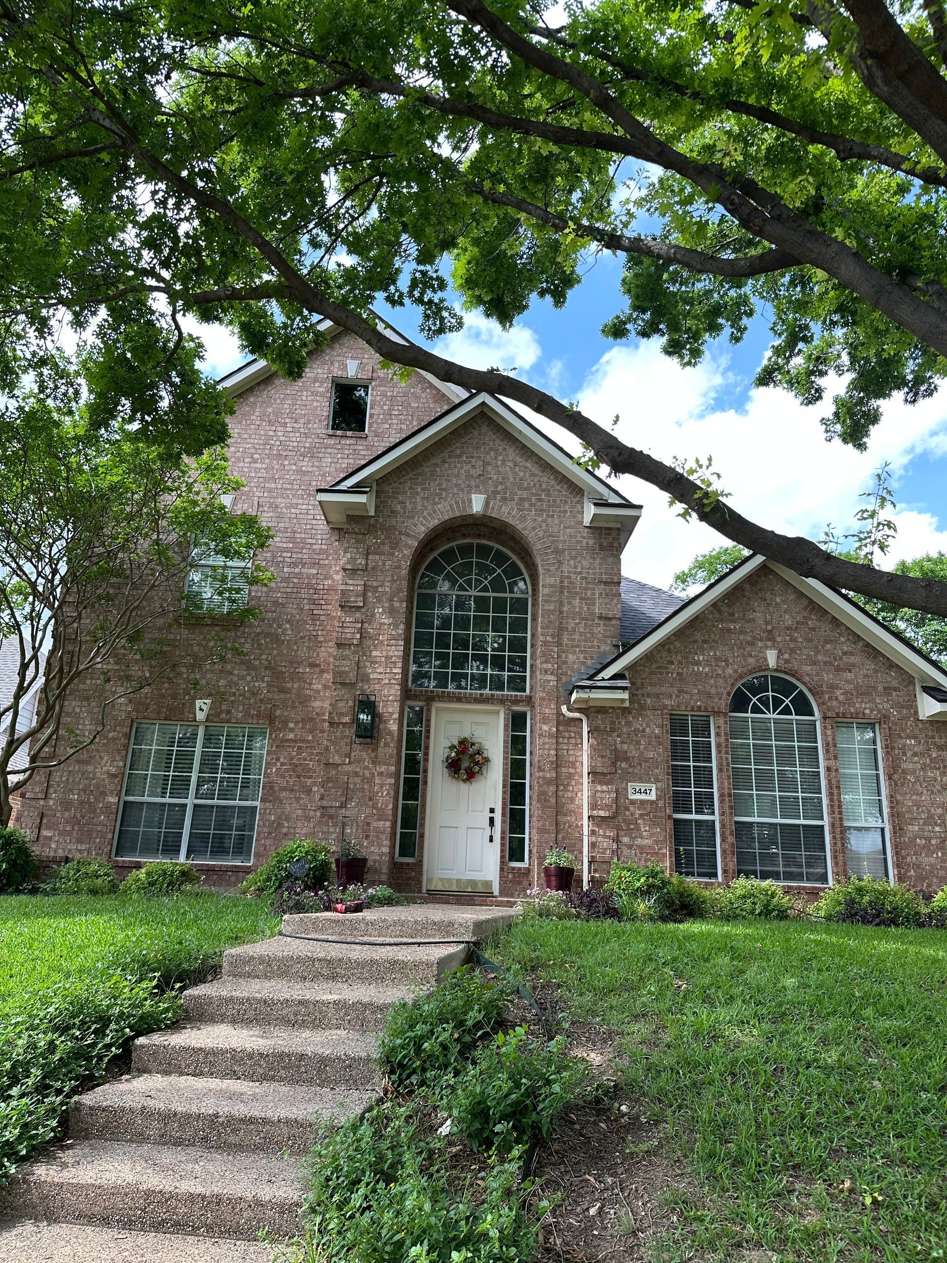 A large brick house with stairs leading up to it and a tree in front of it.