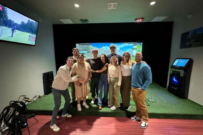 A group of people are posing for a picture in front of a golf simulator.