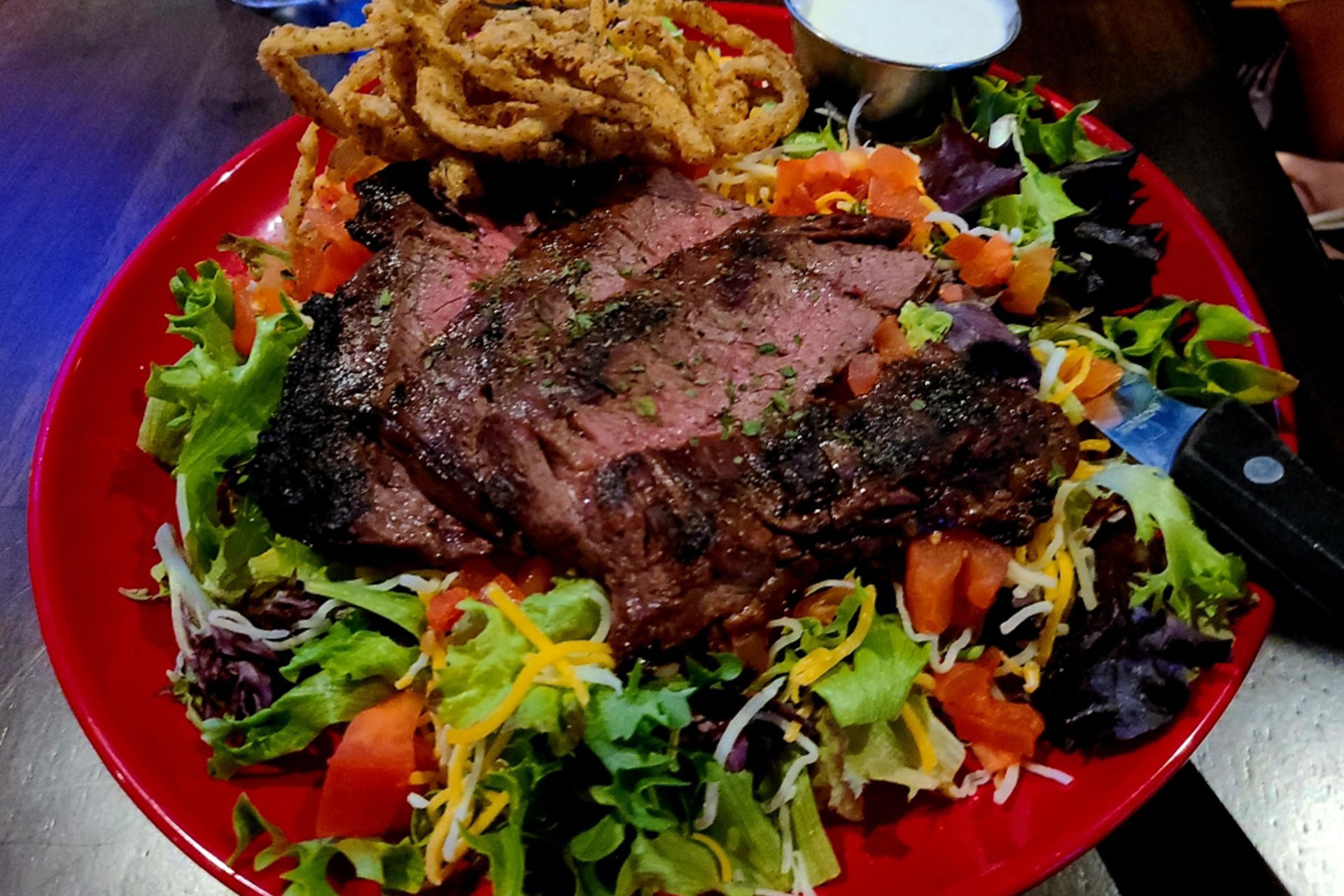 A salad with steak and onion rings on a red plate.