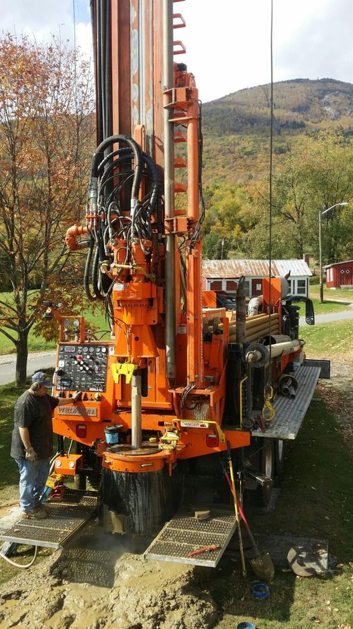 Black water tank and cream pressure tank with pump and pipes, outdoors in a field.