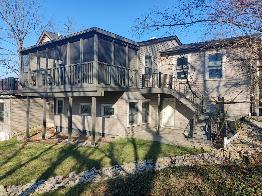 Empty wooden deck beside a house, with railings and leafless trees in bright sunlight.