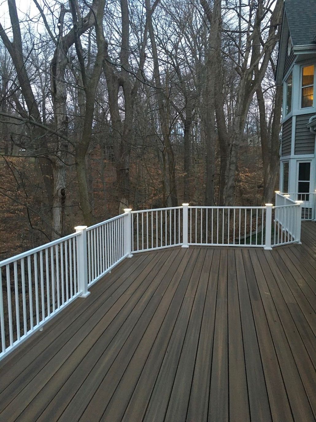 Wooden deck with white railing overlooking leafless trees beside a house