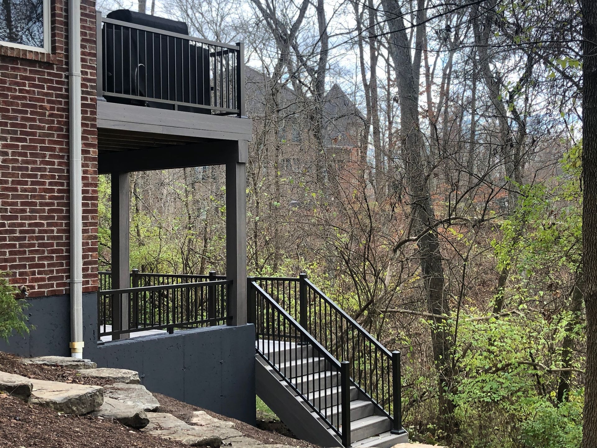 Brick apartment building balcony and black metal stairway beside wooded area.