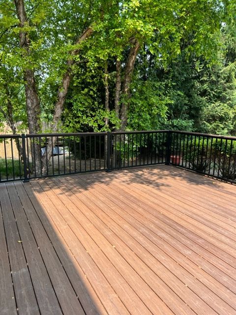 Wooden deck with black railing overlooking a leafy green wooded area