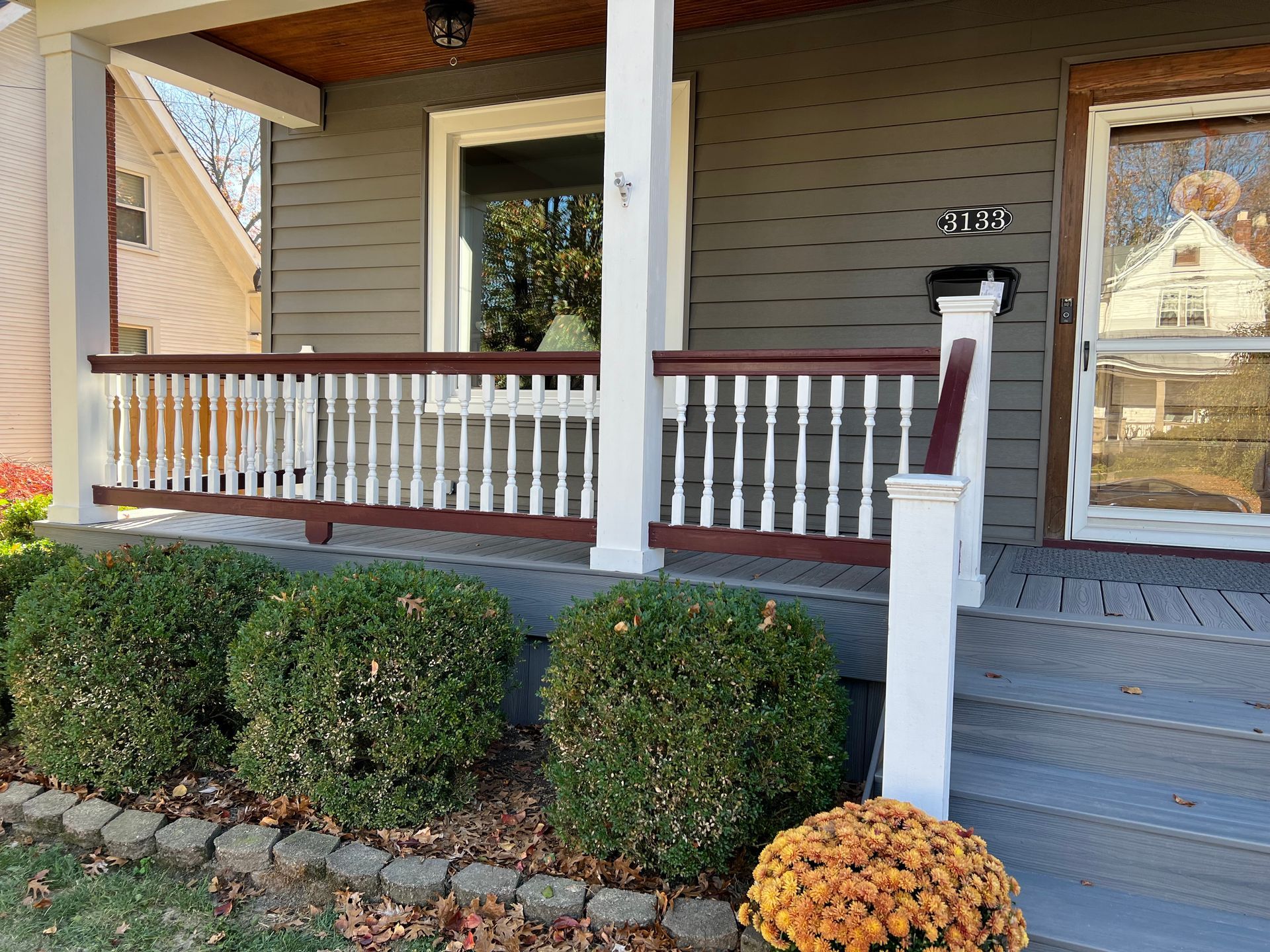 Front porch with white railing, blue steps, and neatly trimmed shrubs in front of a house.