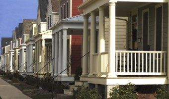 Row of attached suburban houses with front porches and white railings on a sunny day