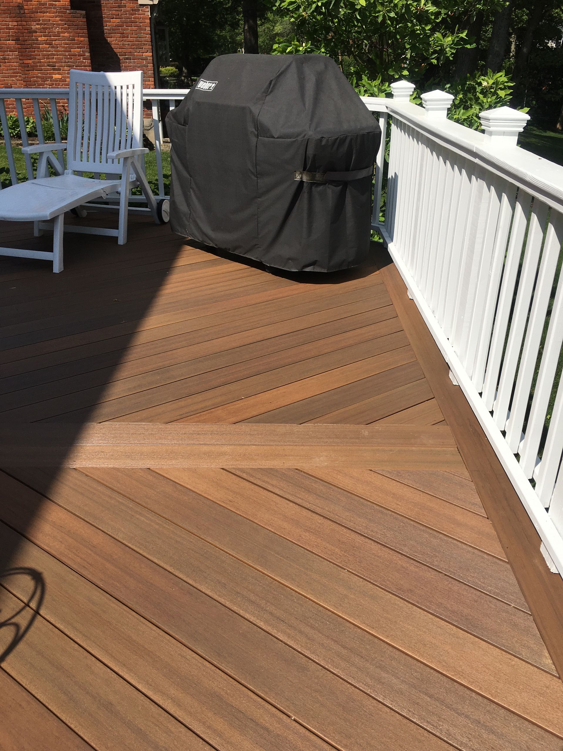 Wooden deck with a covered grill, white railing, and a white chair in sunlight