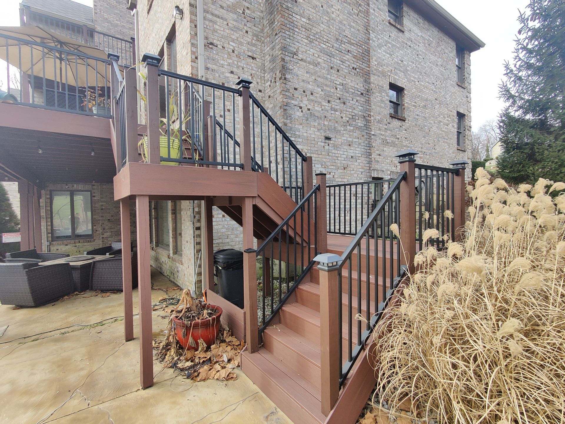 Outdoor wooden staircase with black railings beside a stone house and patio furniture