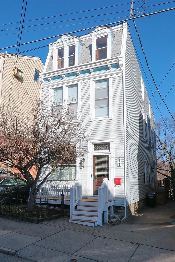 Three-story white house with dormer windows and front steps on a sunny street corner