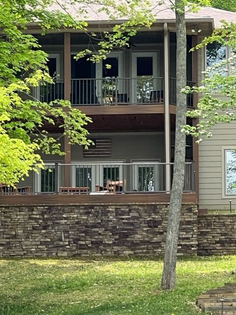 Two-story house with stone porch wall, dark balcony, and trees in the front yard