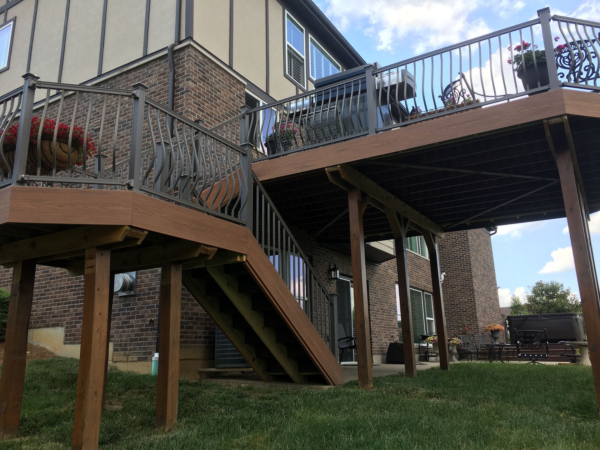 Raised wooden deck with metal railings and stairs beside a brick house in a backyard