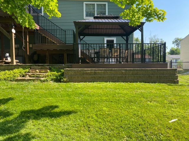 Backyard patio with stairs, black railing, and a covered pergola beside a green lawn