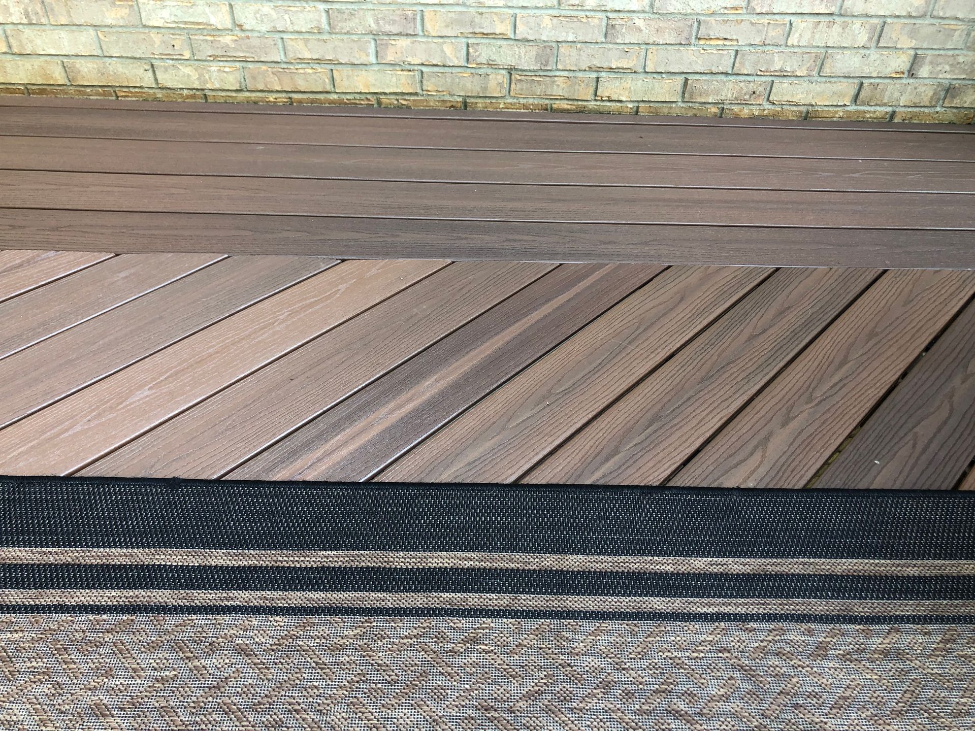 Wooden deck boards beside a brick wall, with a dark metal railing in the foreground