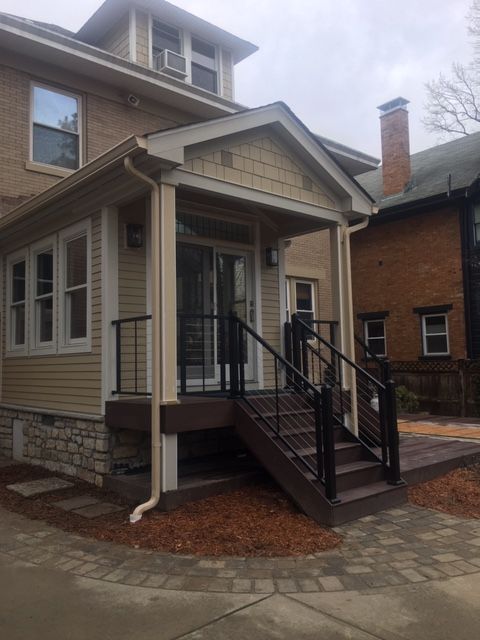 Front porch entrance with stairs and black railing on a beige house exterior