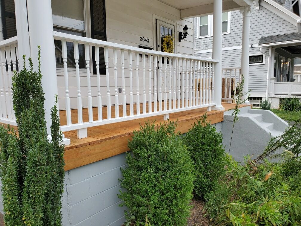 Front porch with white railing, gray steps, and green shrubs beside a house