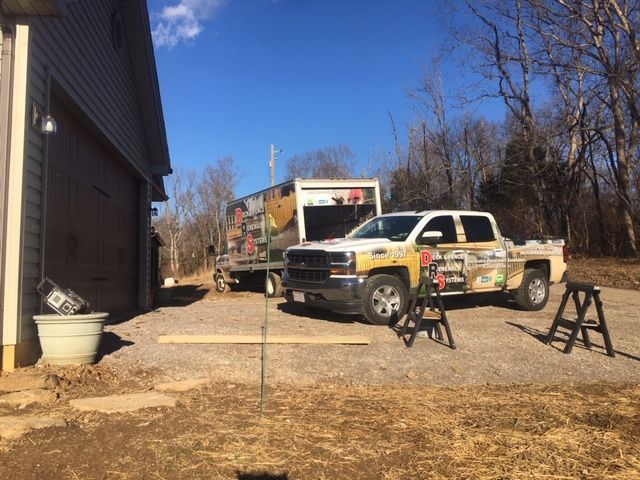 Pickup truck and service truck parked on gravel beside a building, with tools set up outdoors.