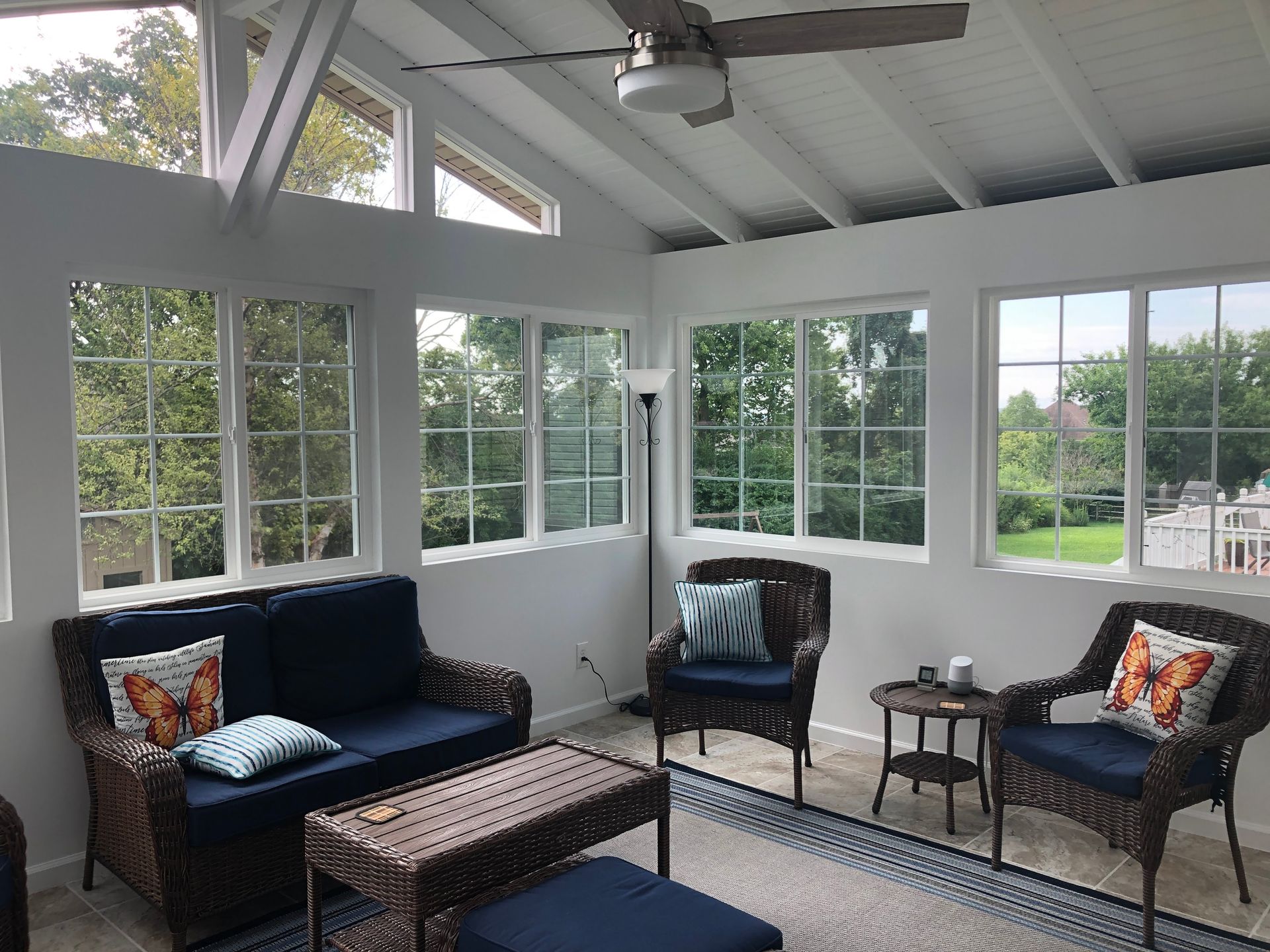 Sunroom with white trim, large windows, navy sofa, wicker chairs, and a glass-top coffee table