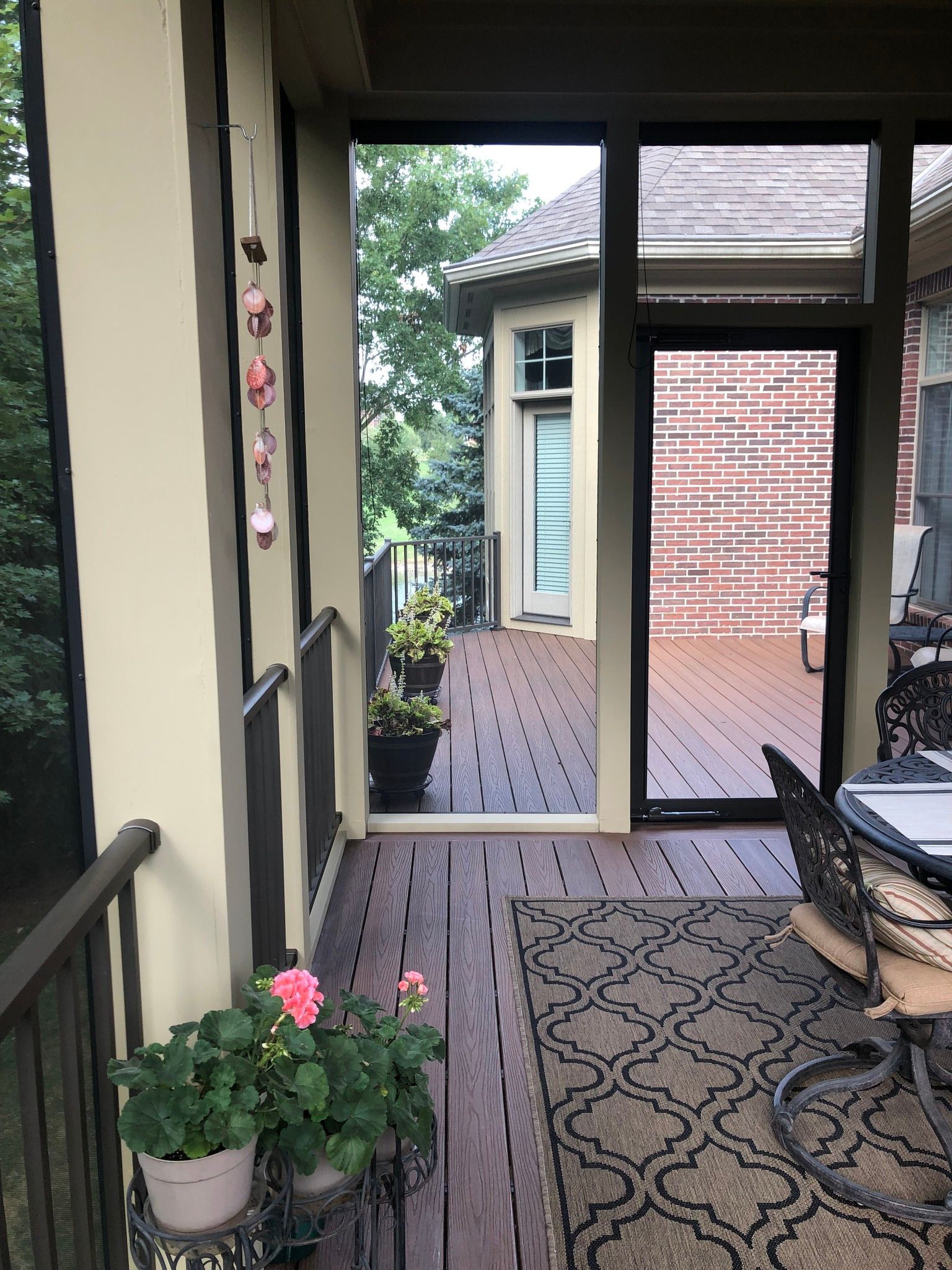 A screened-in porch with a patterned rug, patio furniture, potted flowers, and a doorway leading to an outdoor deck.