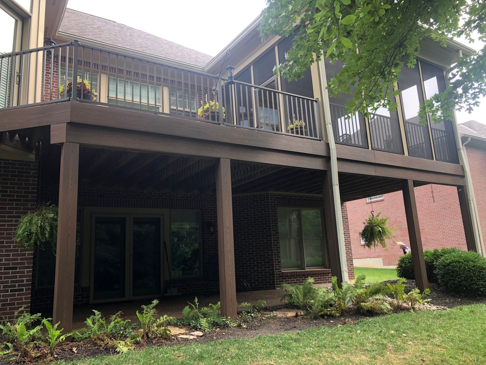 A dark brown multi-level deck and screened-in porch attached to a red brick house overlooking a landscaped lawn.