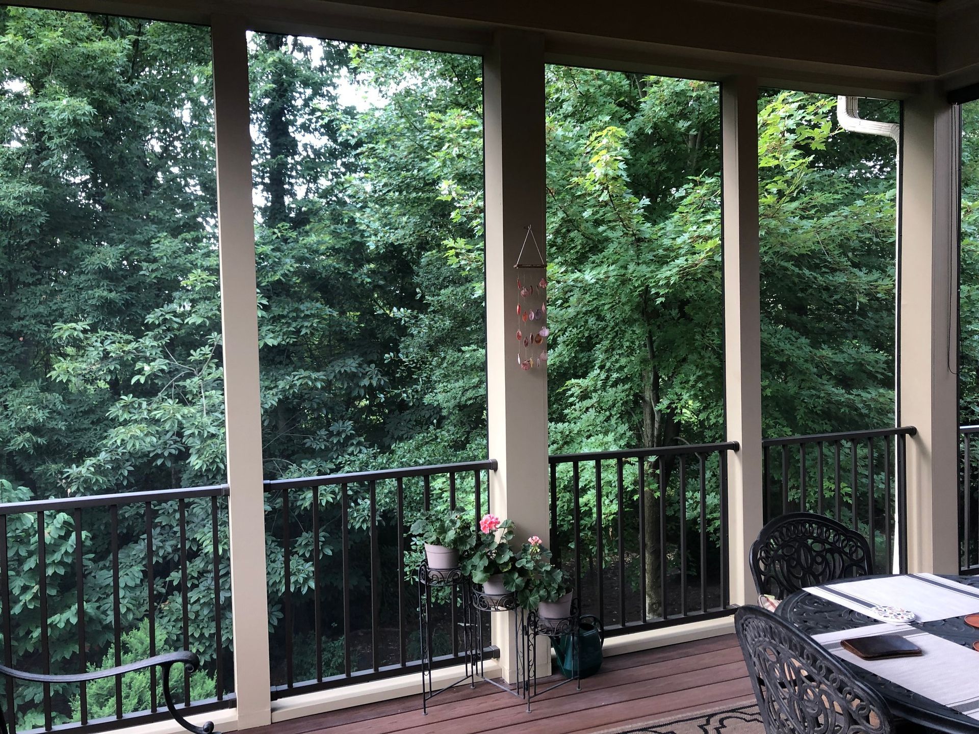 A screened-in porch with a metal railing overlooking a lush forest of green trees.