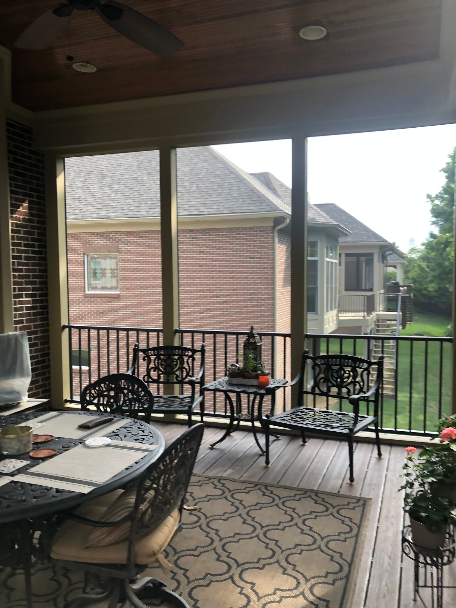 A screened-in deck with metal chairs and a table, overlooking a backyard with neighboring brick houses.