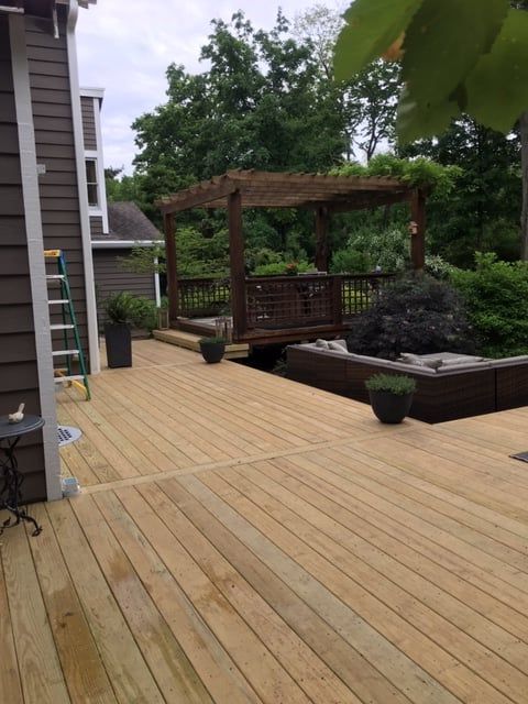 A wooden deck with a built-in seating area and a pergola, viewed from the side of a brown-sided house.