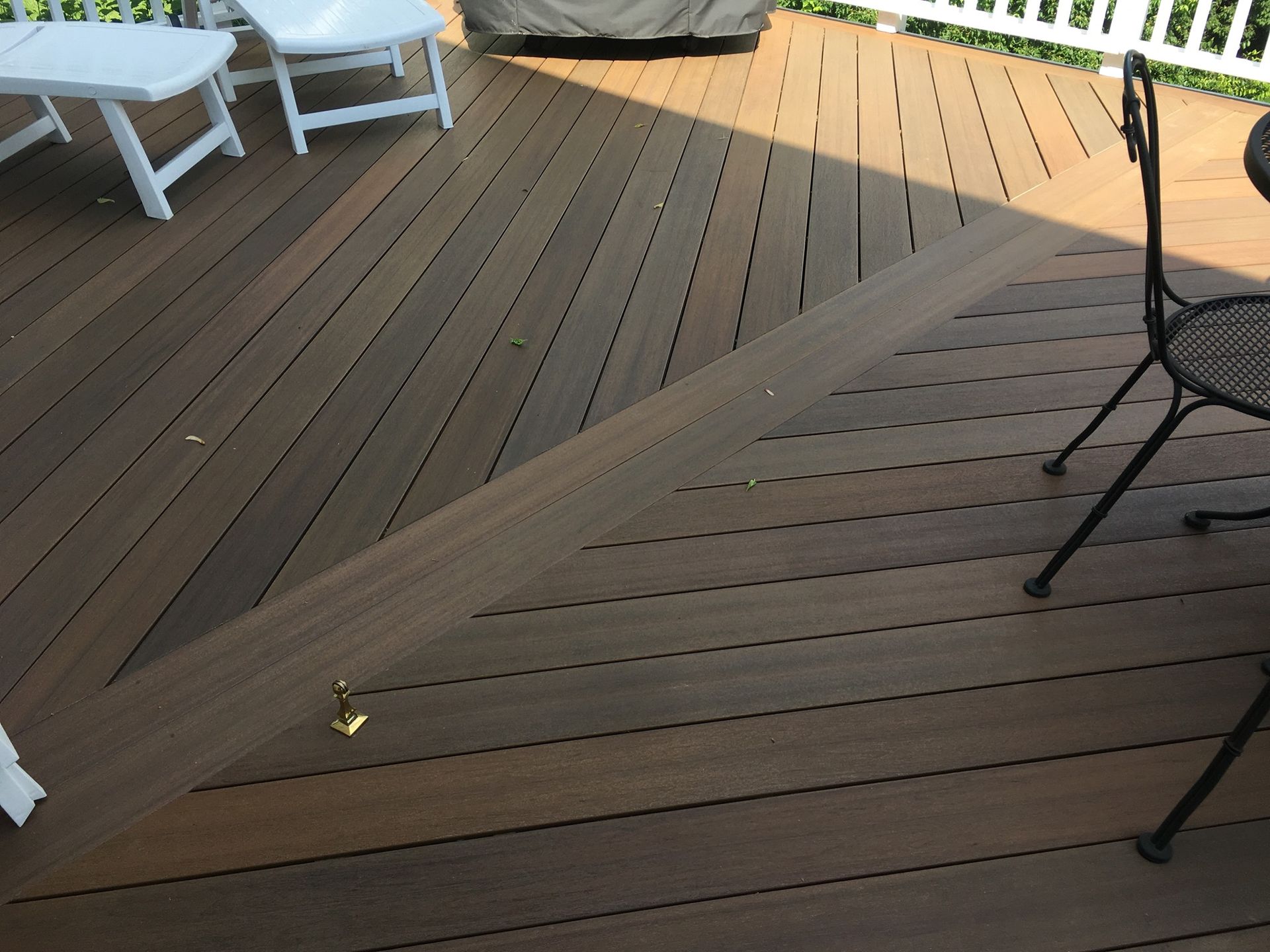 A brown wooden deck with a diagonal board layout, featuring a white chair and a dark metal chair on the surface.