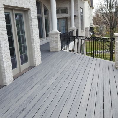 A light gray composite deck with a black metal railing outside a house with white brick walls and white columns.