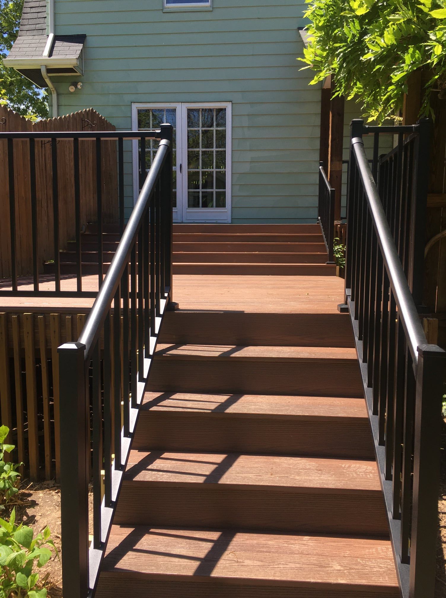 Outdoor wooden staircase with black railings leading up to a light green house with white French doors.